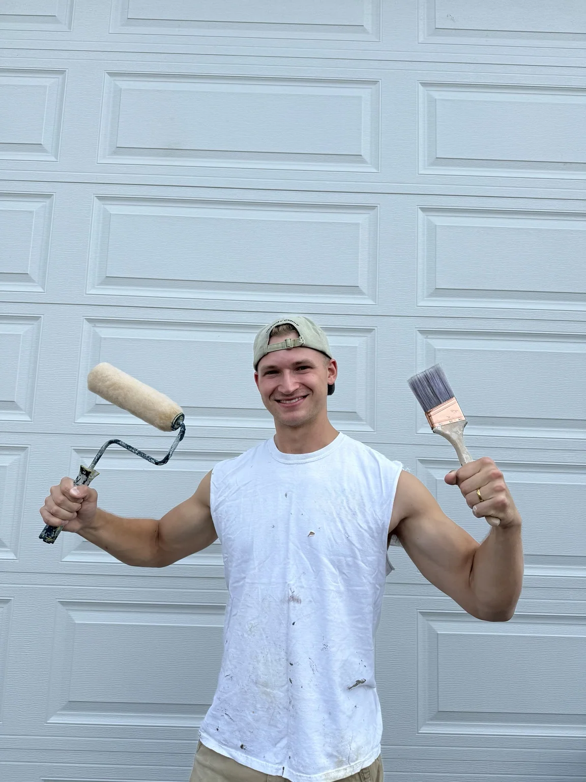 Me smiling while holding a paint roller and brush in front of a white garage door.