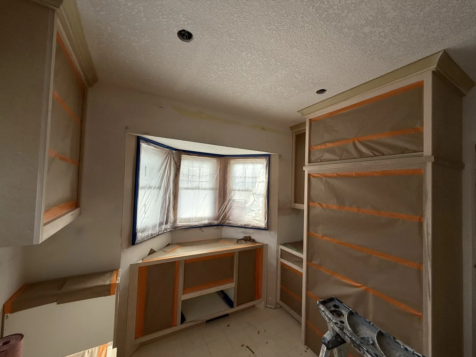 Kitchen cabinets masked and prepared before a gray cabinet finishing project.